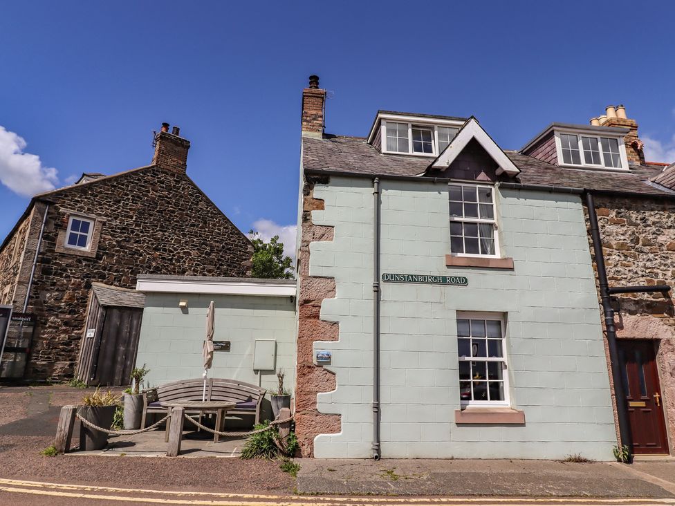 A house with a bench and sign on Dunstanburgh Road at Marie's Cottage in Craster