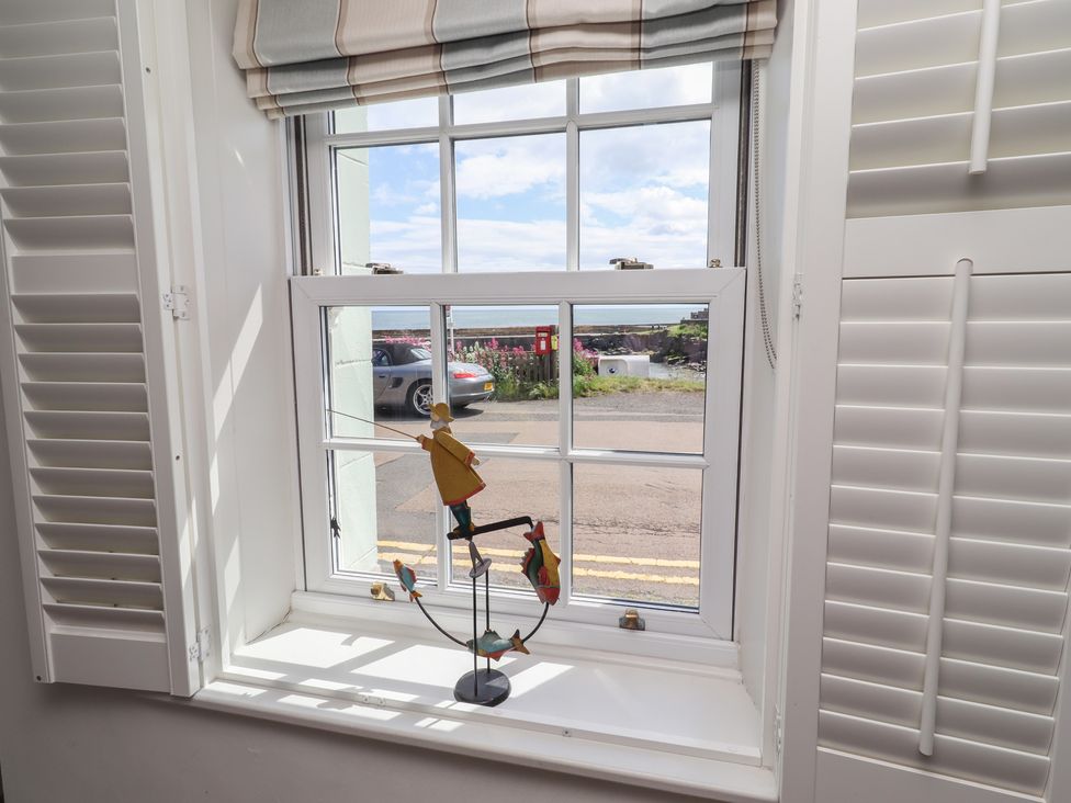 A window with a fishing figurine in the living room at Marie's Cottage in Craster