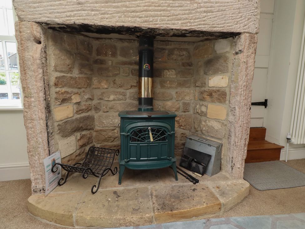 A living room with a wood stove in a stone fireplace at Marie's Cottage in Craster