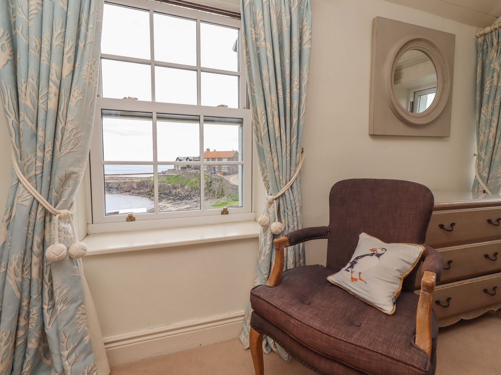 A sitting room with a window and a chair at Marie's Cottage, Craster