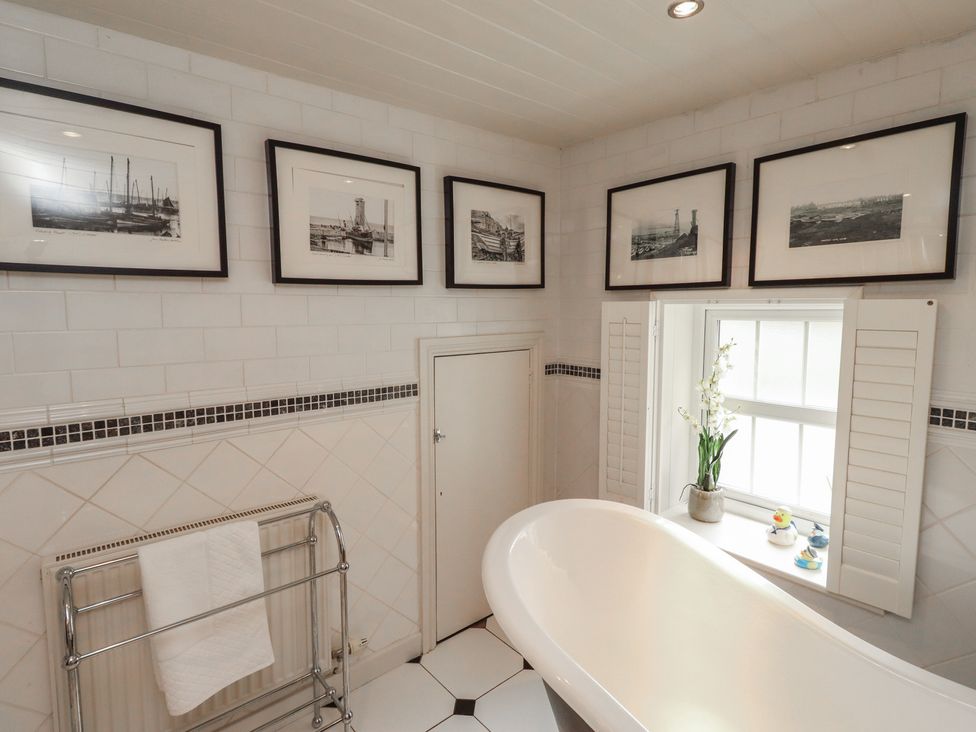 A bathroom featuring a bathtub, photographs on the wall and a window at Marie's Cottage in Craster