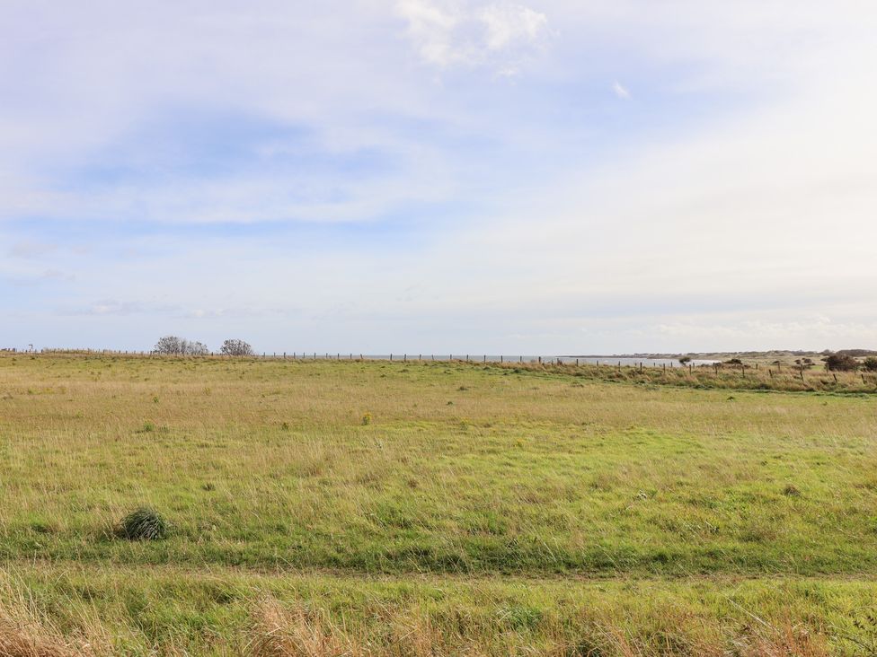 A grass field with a fence and water in the distance at Beach View in Seahouses