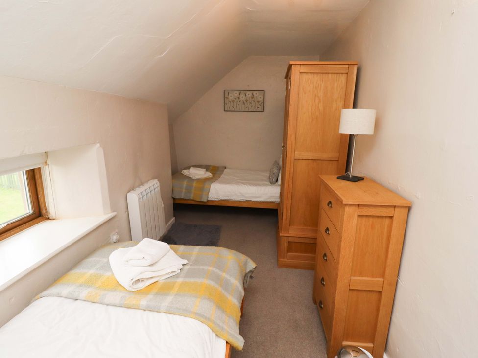 A bedroom with two beds and wooden furniture at Heather Cottages - Brent Goose in Bamburgh