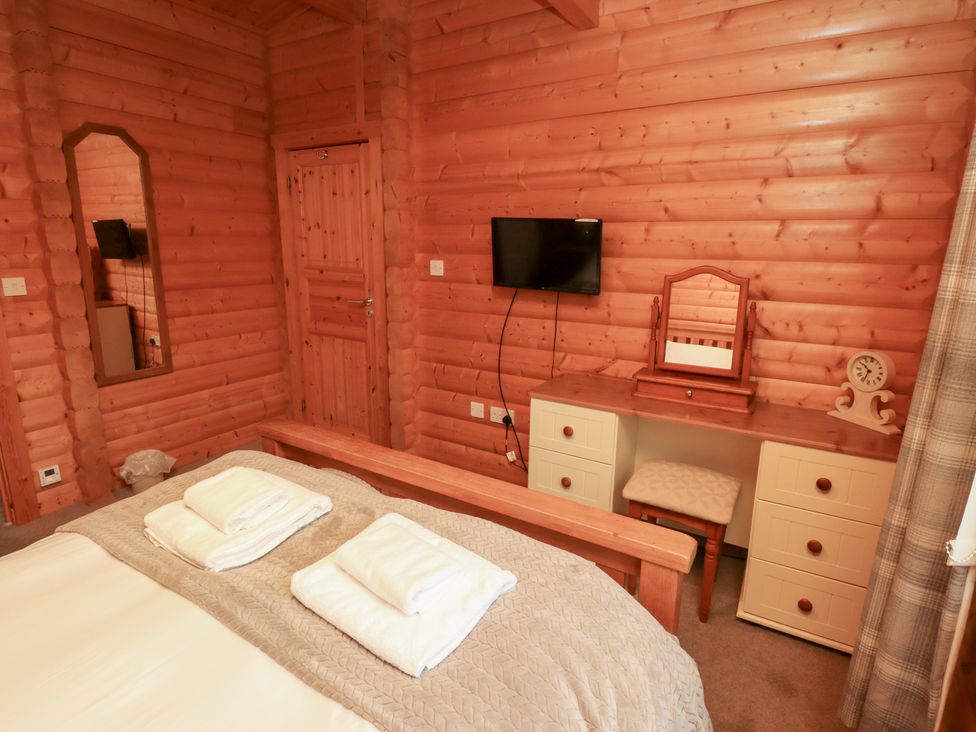 A bedroom with wooden walls, a bed with towels, a dressing table and a television at Heather Cottages - Brown Owl in Bamburgh