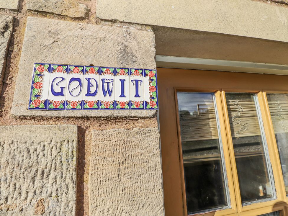 A sign labeled Godwit on a stone wall near a window at Heather Cottages - Godwit in Bamburgh