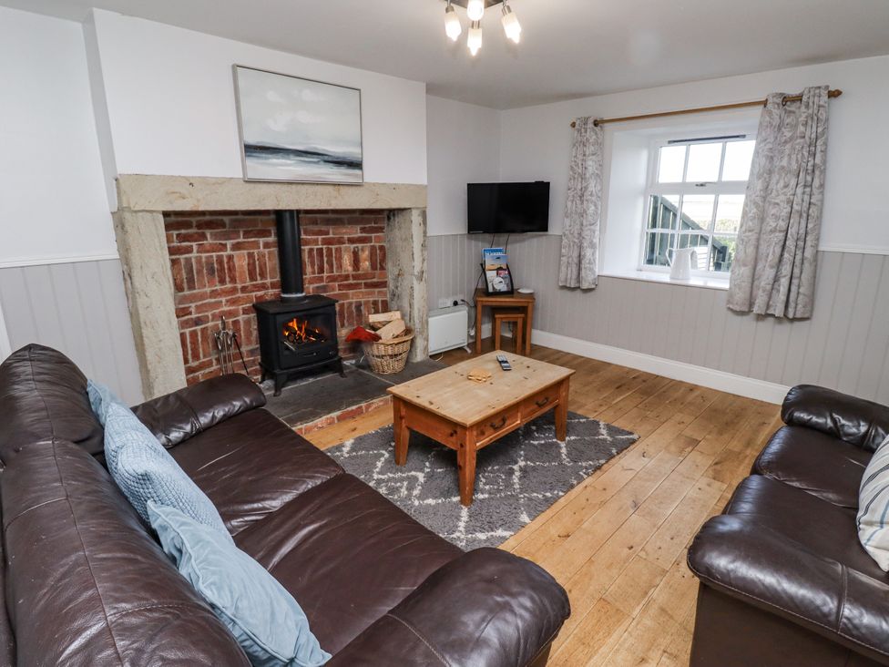 A living room with a wood stove and sofa at Heather Cottages - Godwit in Bamburgh