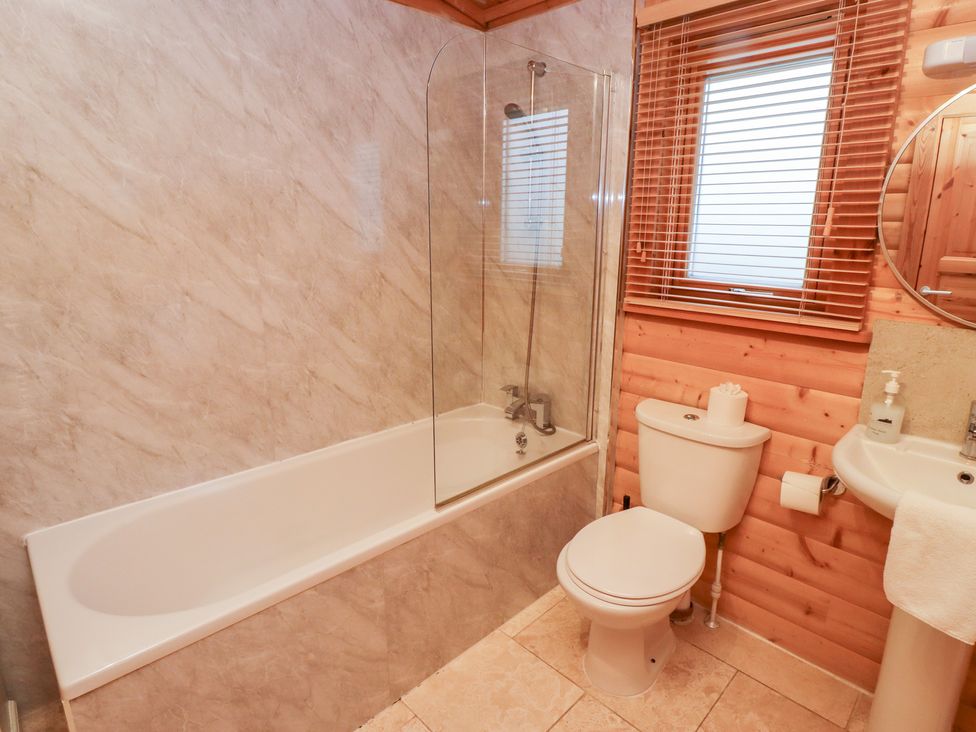 A bathroom with a bathtub, shower, toilet and sink at Heather Cottages - Grey Heron in Bamburgh