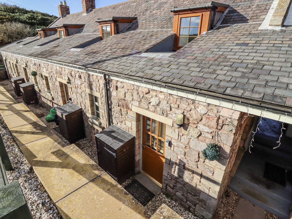 An outdoor view of a stone building with windows and pathways at Heather Cottages - Plover in Bamburgh