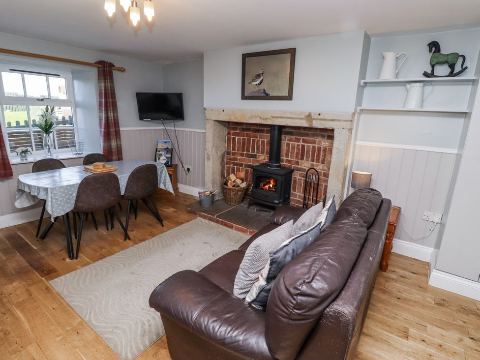 A living room with a sofa, dining table, and fireplace at Heather Cottages - Plover in Bamburgh