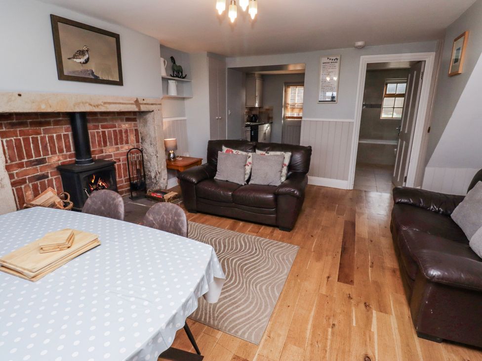 A living room with a fireplace, dining table, and sofa at Heather Cottages - Plover in Bamburgh