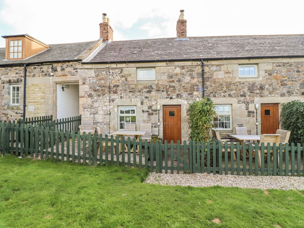 An outdoor area with a stone wall and furniture at Heather Cottages - Plover in Bamburgh