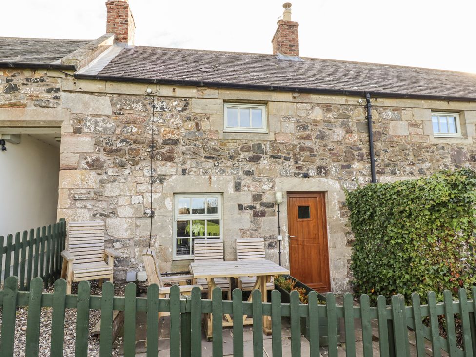 An outdoor area with a wooden table and chairs near the entrance at Heather Cottages - Plover in Bamburgh