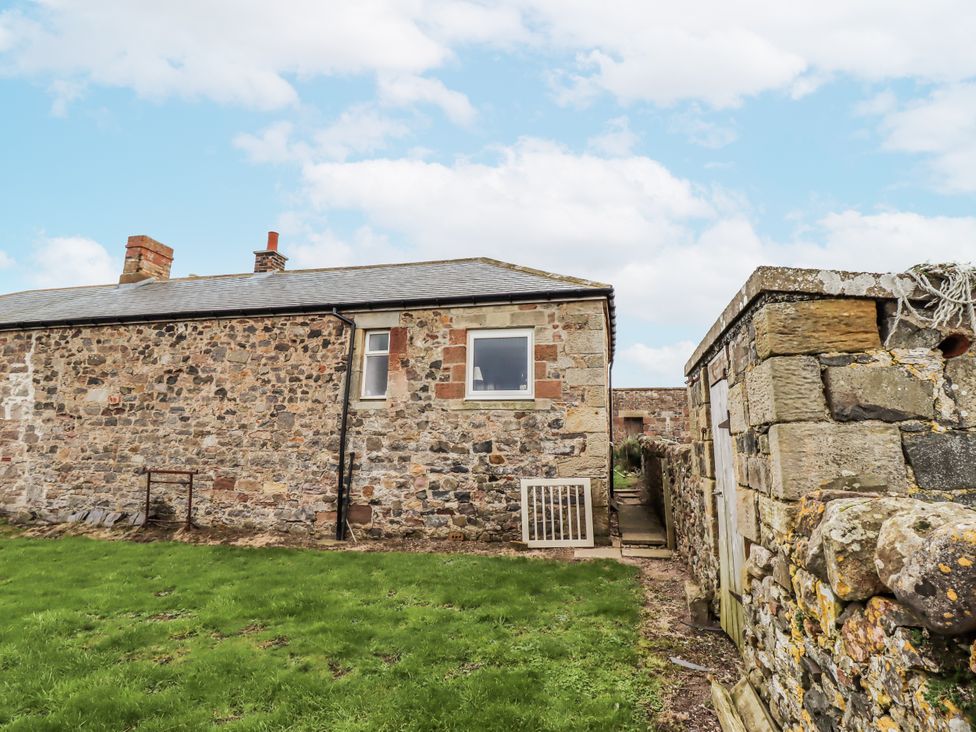 Exterior view of a stone cottage with a grassy area at Kittiwake Cottage, Budle Bay