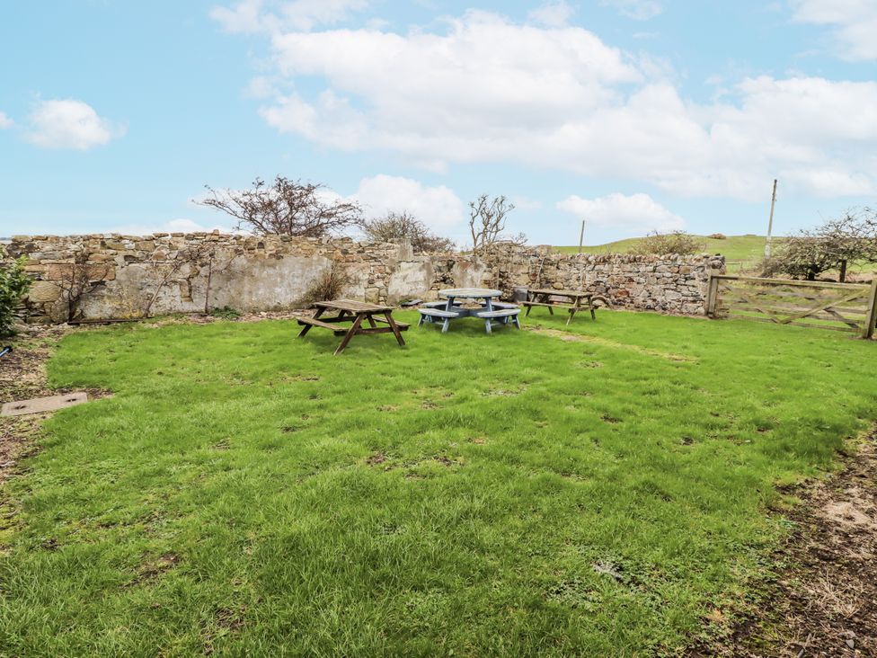 A garden area with picnic tables and a stone wall at Kittiwake Cottage, Budle Bay