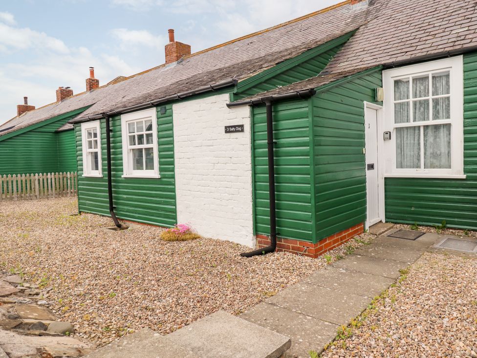 A green wooden cottage with white windows and door on a gravel yard at Salty Dog in Bamburgh