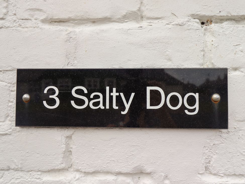 A black plaque with white text saying 3 Salty Dog on a white brick wall at Salty Dog in Bamburgh