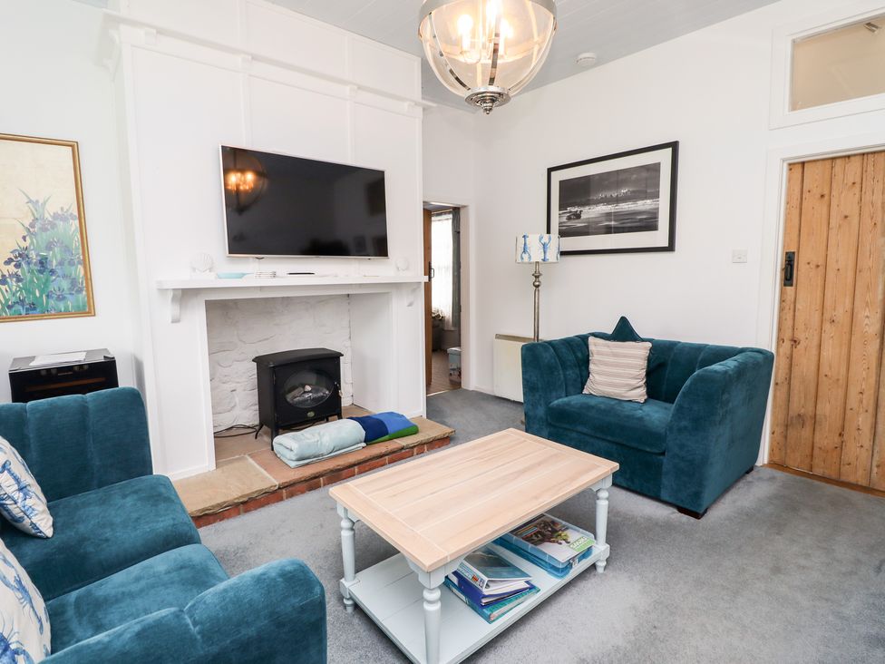 A living room with two blue armchairs a wooden door a fireplace with a TV above and a coffee table at Salty Dog in Bamburgh