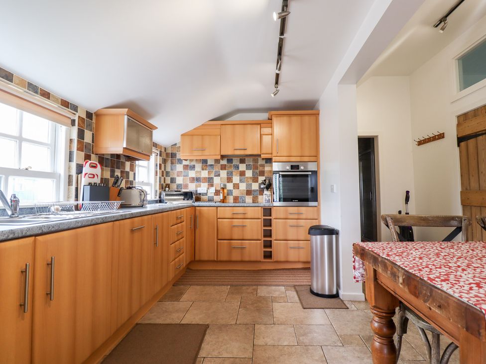 A kitchen with wooden cabinets and tiled backsplash and a wooden table with a patterned tablecloth at Salty Dog in Bamburgh