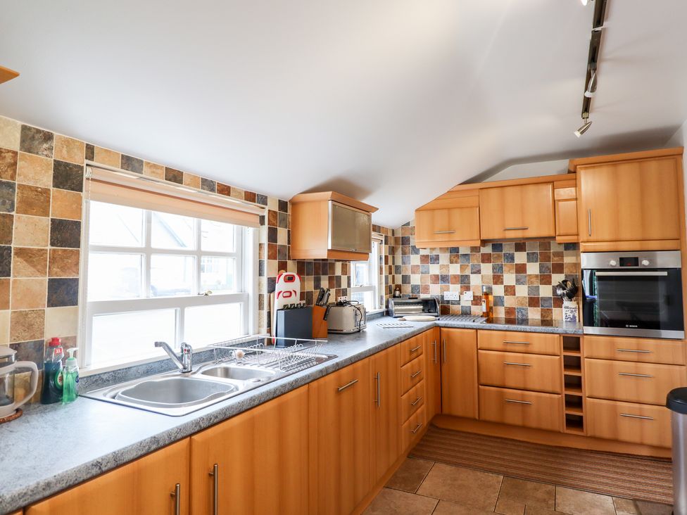 A kitchen with wood cabinets tiled backsplash stainless steel sink and built in oven at Salty Dog in Bamburgh