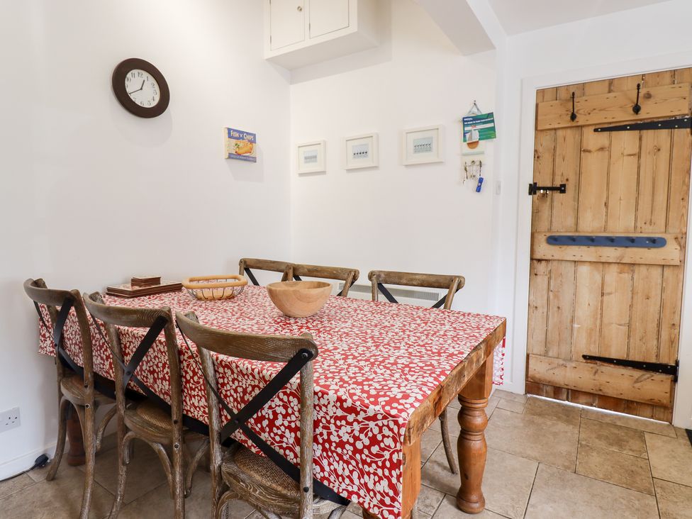 A dining area with a wooden table covered with a red and white tablecloth surrounded by six wooden chairs and a wooden door at Salty Dog Bamburgh