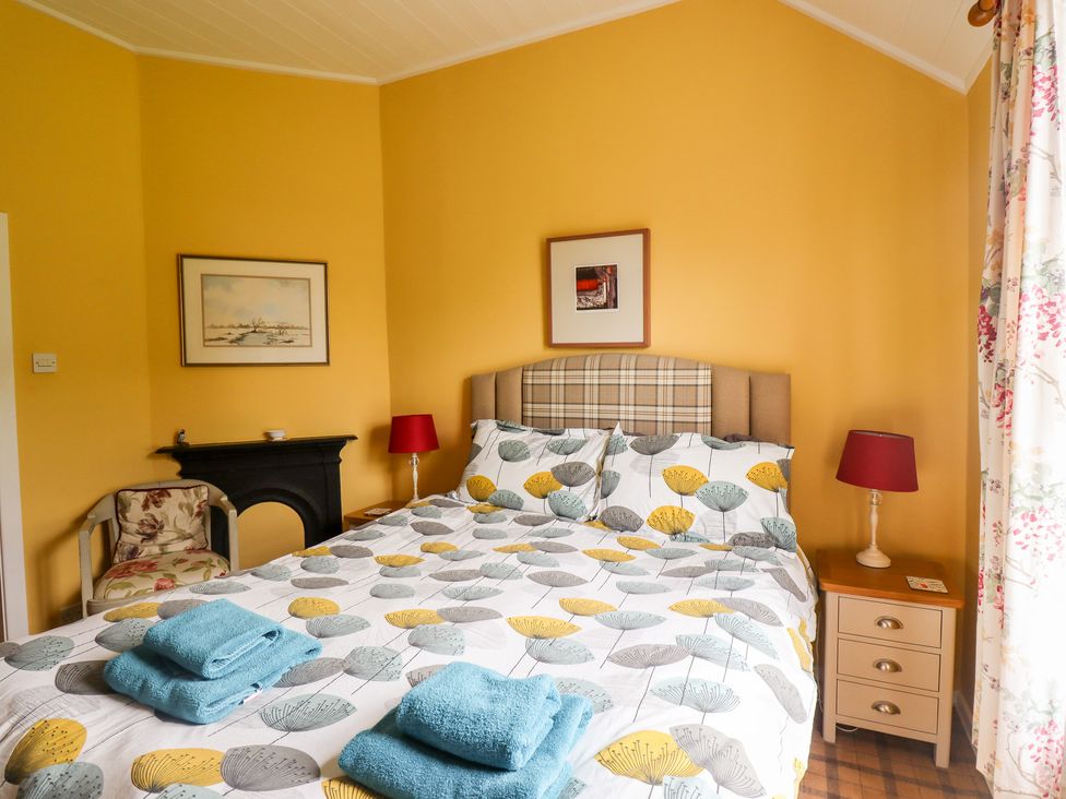 A bedroom with a double bed with patterned bedding blue towels on the bed a chair bedside tables with red lamps floral curtains and yellow walls at Salty Dog Bamburgh