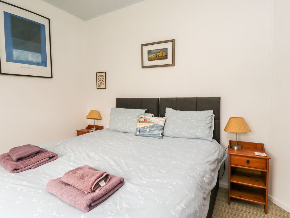 A bedroom with a double bed two bedside tables and lamps and framed pictures on the wall at Salty Dog in Bamburgh