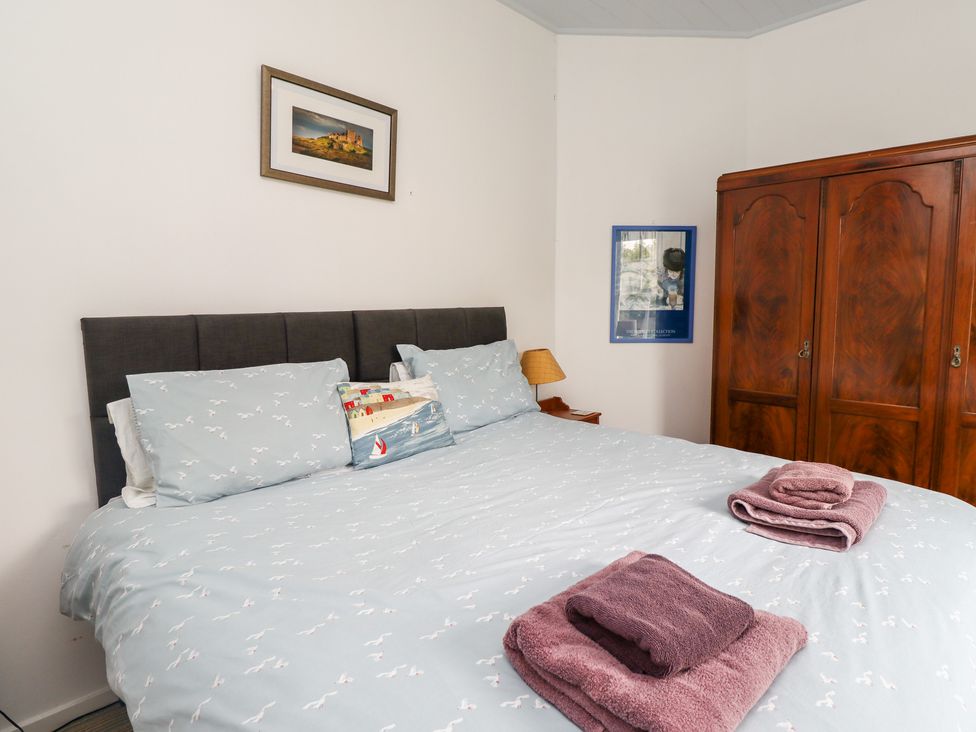 A bedroom with a double bed and folded towels on the bed beside a wooden wardrobe at Salty Dog in Bamburgh