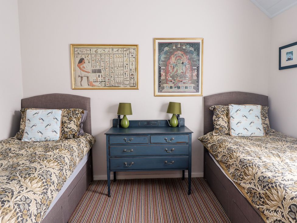 A bedroom with two single beds a blue dresser with two green lamps and framed artwork on the wall at Salty Dog in Bamburgh