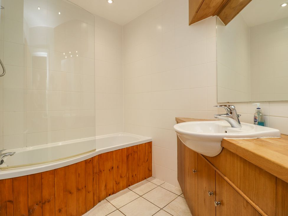 A bathroom with a bathtub that has a wooden panel and a sink with a wooden cabinet at Salty Dog in Bamburgh