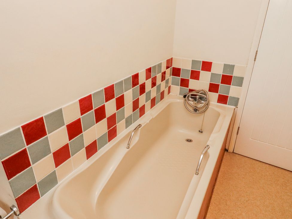 A bathroom with a bathtub and tiled wall at St Marys Cottages No4 Low Newton-by-the-Sea
