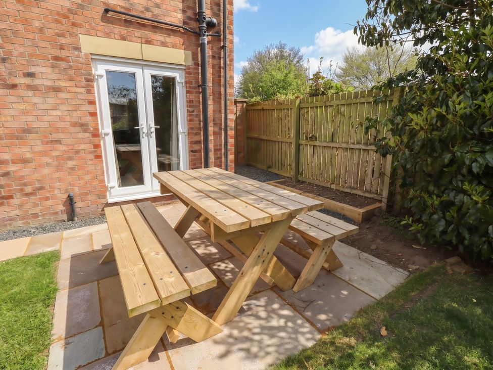 A garden with a wooden table and benches at Sugar Sands in Longhoughton