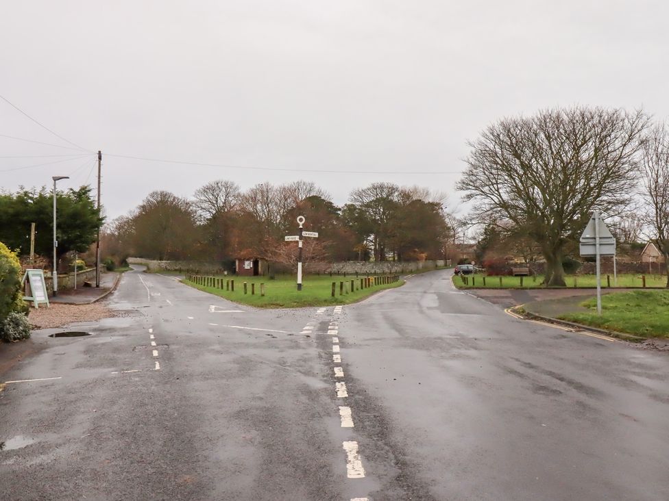 A road intersection with a signpost and trees at Wayside Cottage in Newton-by-the-Sea