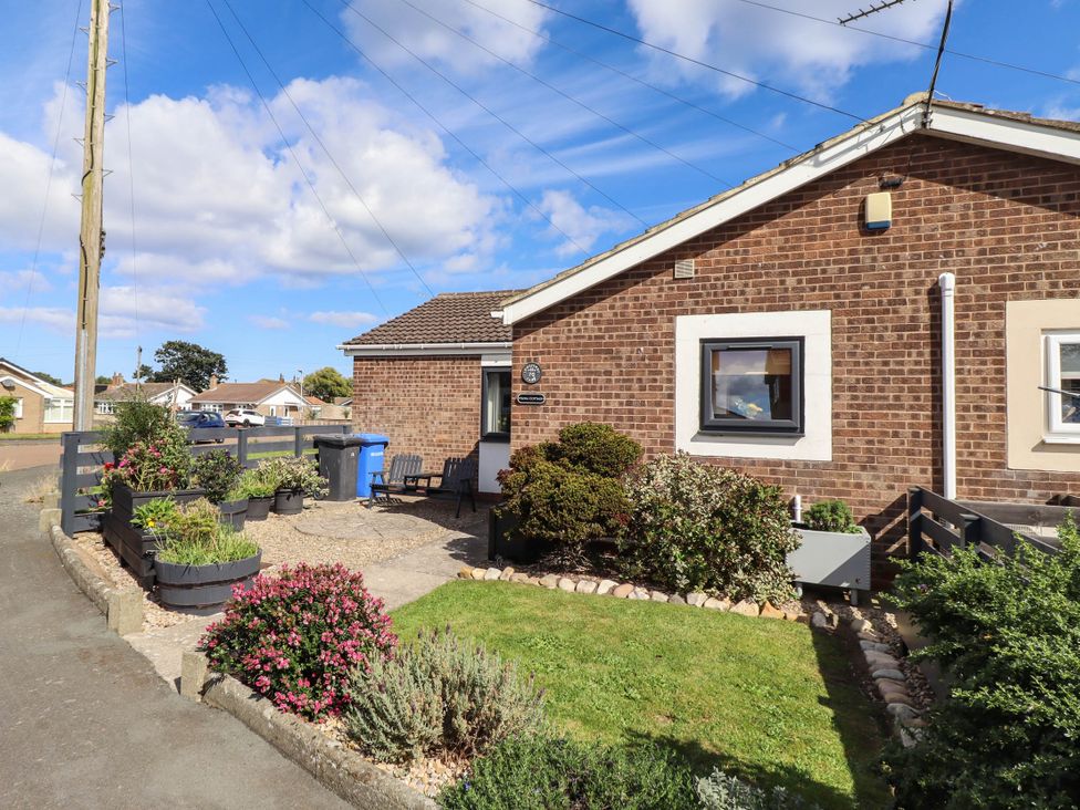 An outdoor area with flower beds and a house at Flora Cottage Beadnell