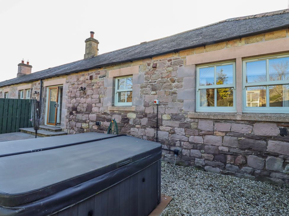 An outdoor view of a house with a hot tub and stone walls at Greenfinch, Lucker