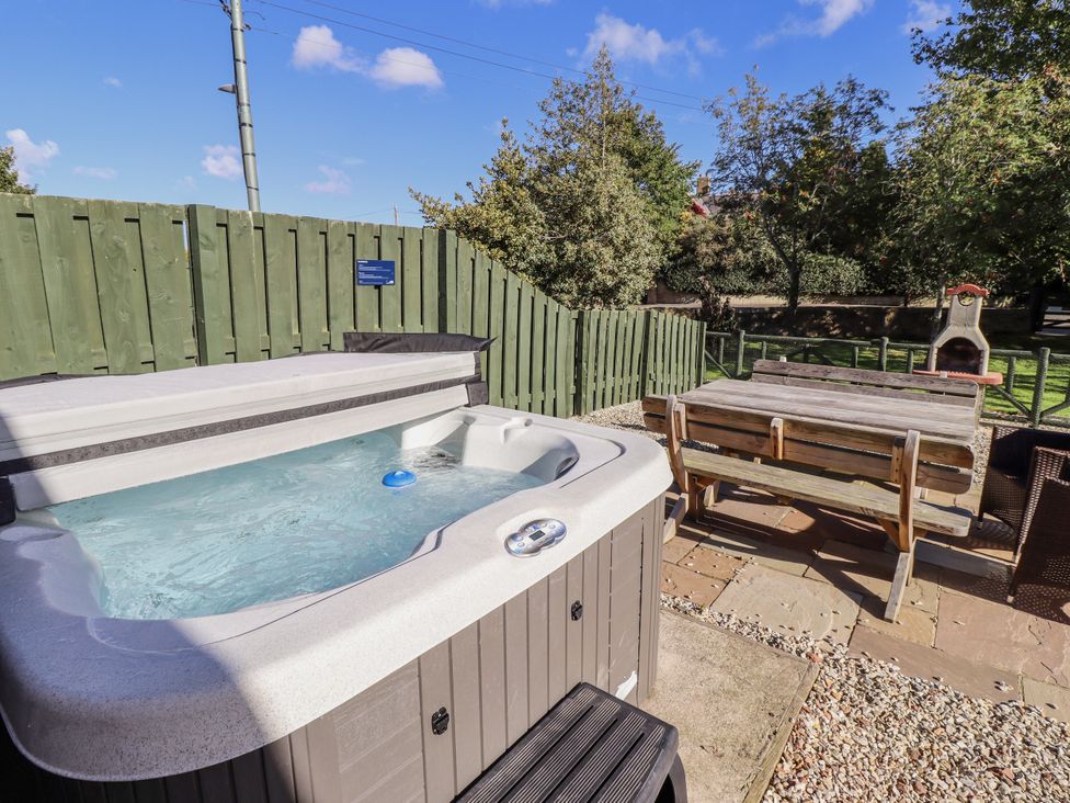 A hot tub with an outdoor table and wooden bench at Rosefinch in Lucker