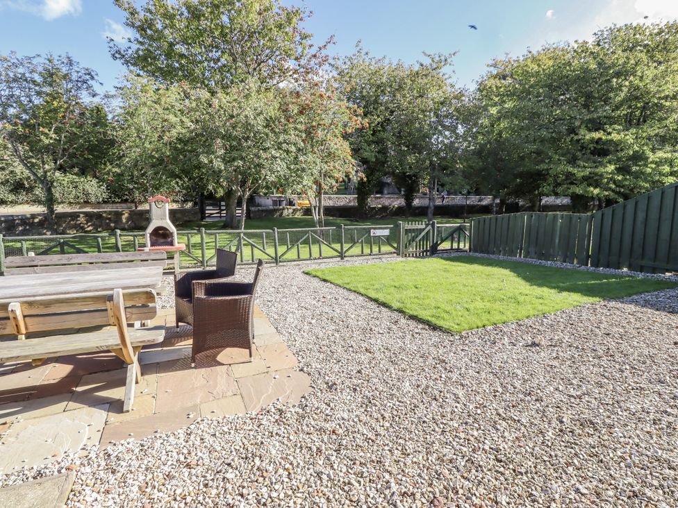 A garden with gravel, grass, table, chairs and barbecue at Rosefinch in Lucker