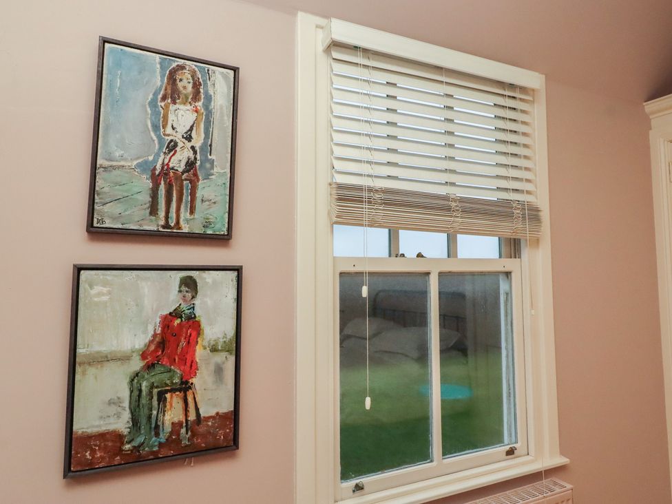 A wall with two paintings and a window with blinds at Armstrong Cottages No6 Bamburgh