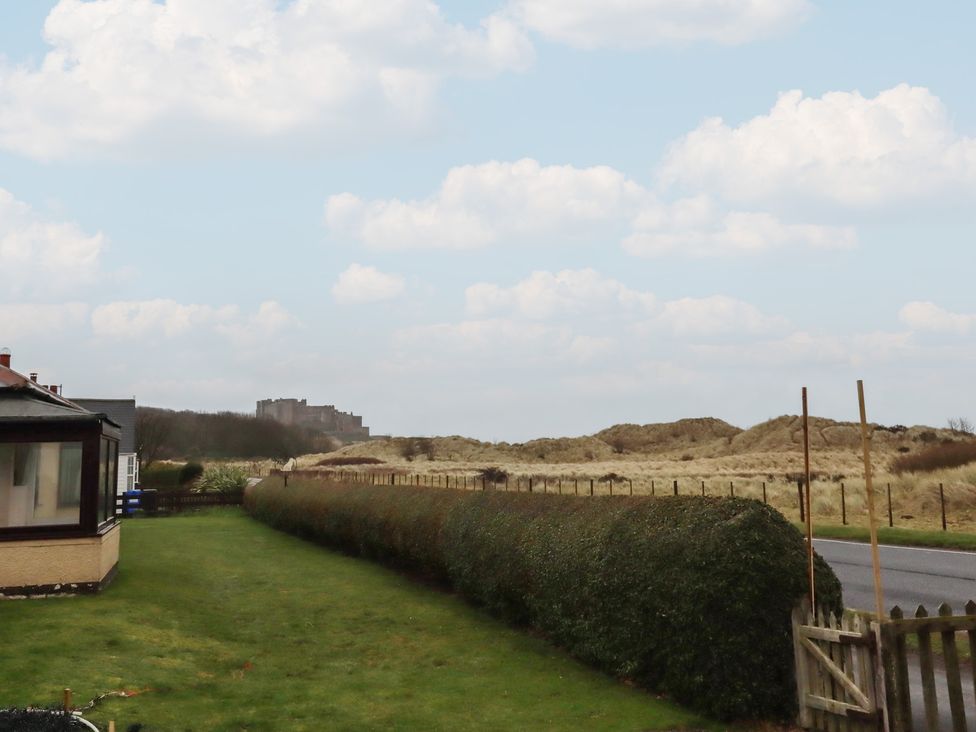 A view of a castle in the distance with a hedge and road at Armstrong Cottages No6 Bamburgh