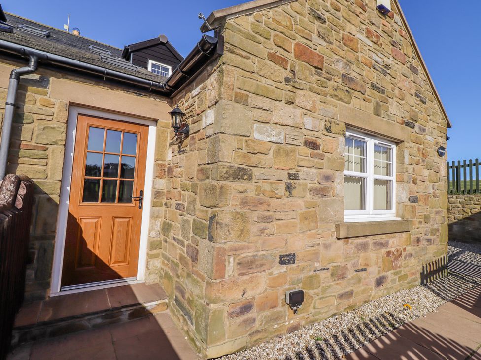 An outdoor area with a stone wall and door at Goosander in Bamburgh