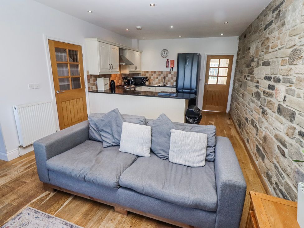 A living room with a sofa and kitchen area at Goosander in Bamburgh