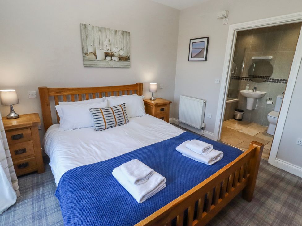 A bedroom with a bed, nightstands, and an ensuite bathroom at Goosander in Bamburgh