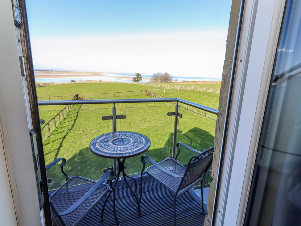 A balcony with table and chairs overlooking a green field at Goosander in Bamburgh