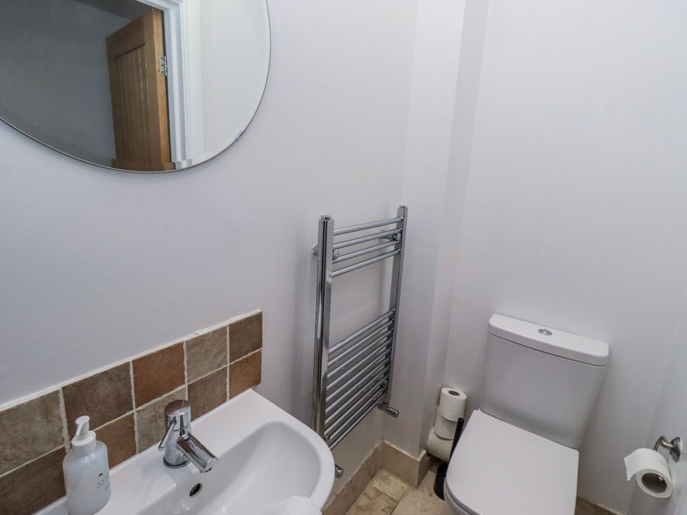 A bathroom with a mirror, sink, towel rail, and toilet at Jackdaw in Bamburgh
