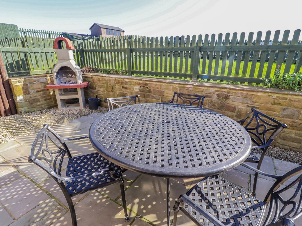 A garden with a table and chairs near a barbecue at Jackdaw in Bamburgh