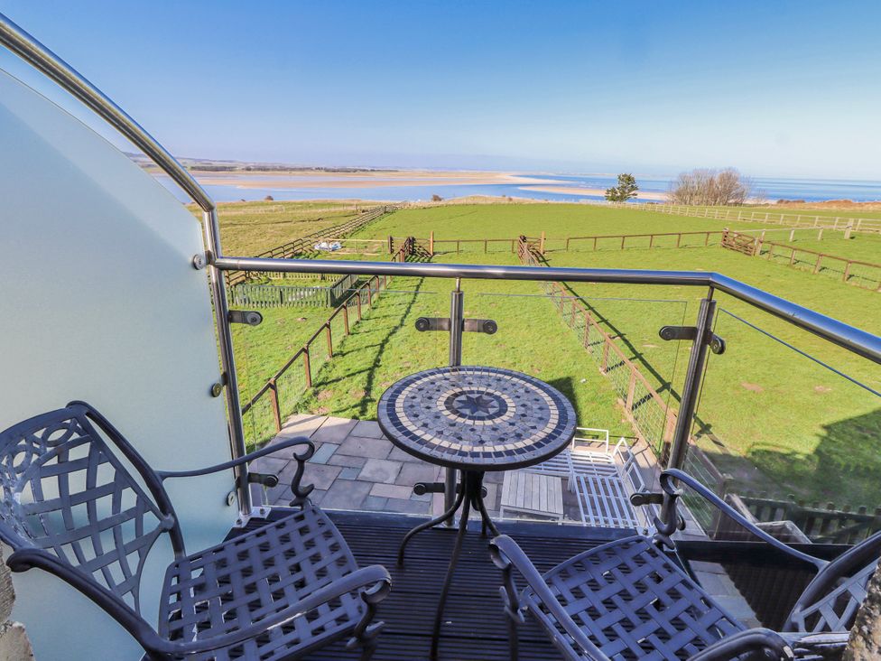 A balcony with a table and chairs overlooking grass fields at Jackdaw in Bamburgh