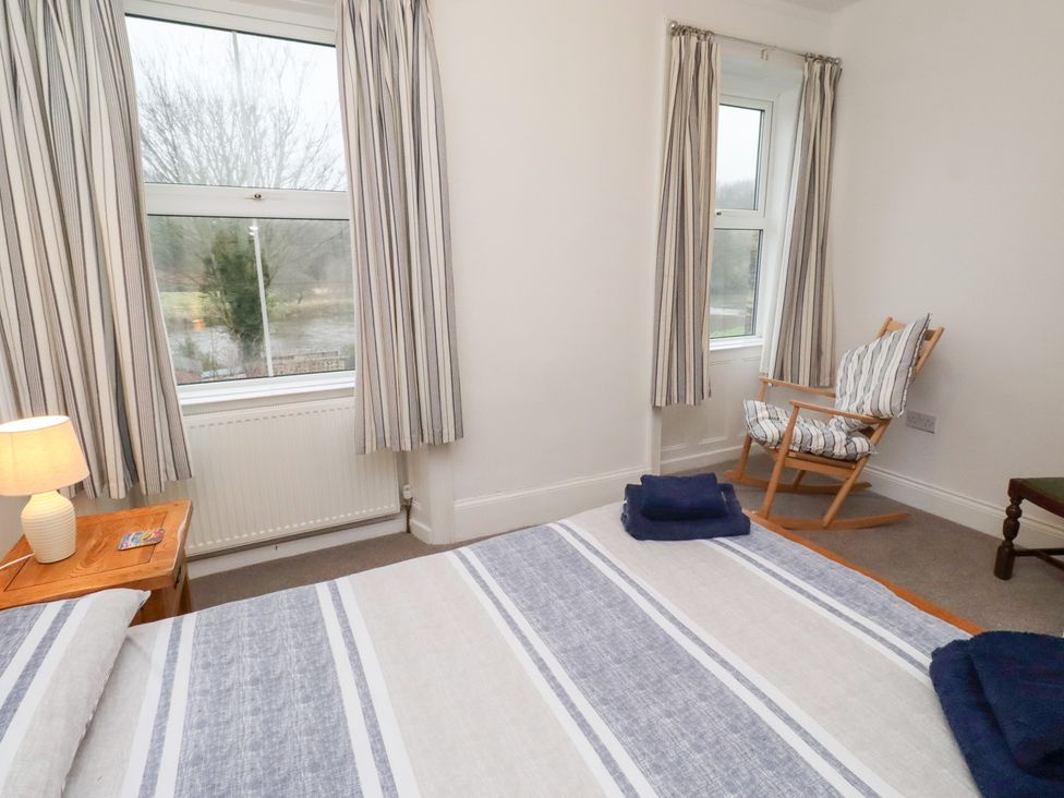 A bedroom with a bed, a rocking chair, and a window at Riverside Cottage in Warkworth
