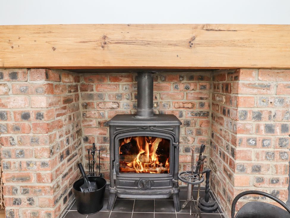 A wood burning stove with fire inside set in a brick fireplace with fire tools and bucket at Jara in Bamburgh