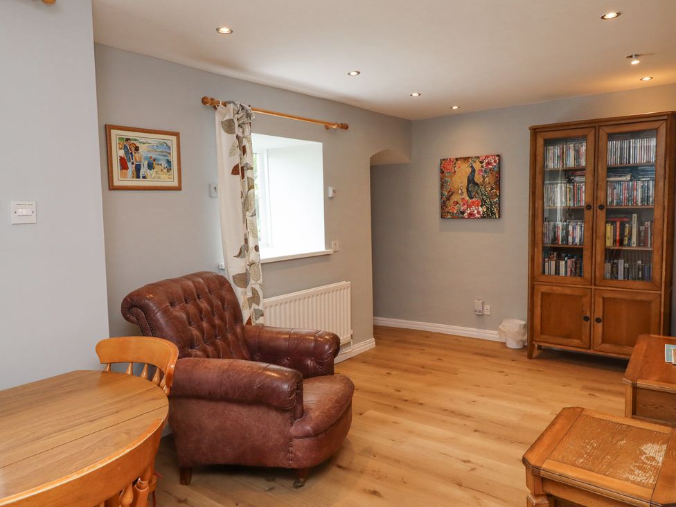 A living room with a brown leather armchair a wooden round table and chairs a wooden cabinet with glass doors and a peacock painting on the wall at Jara Bamburgh