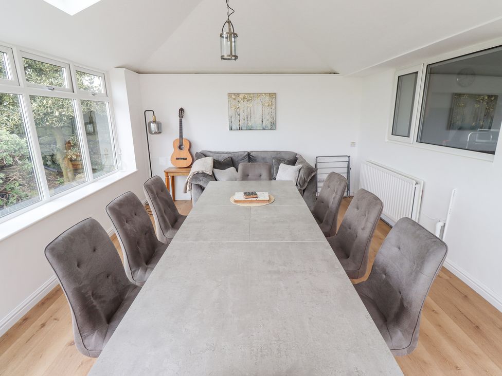 A dining room with a long table surrounded by chairs and a sofa with guitar on a side table at Jara in Bamburgh