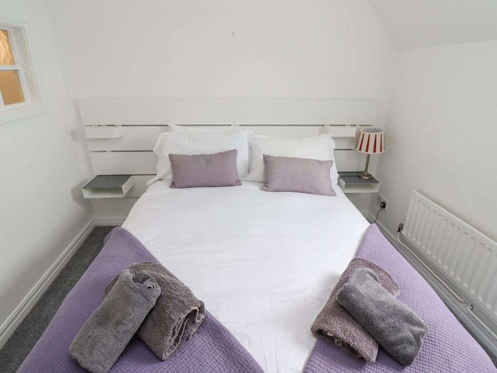 A bedroom with a double bed with white bedding and purple blankets with purple pillows and towels at Jara in Bamburgh